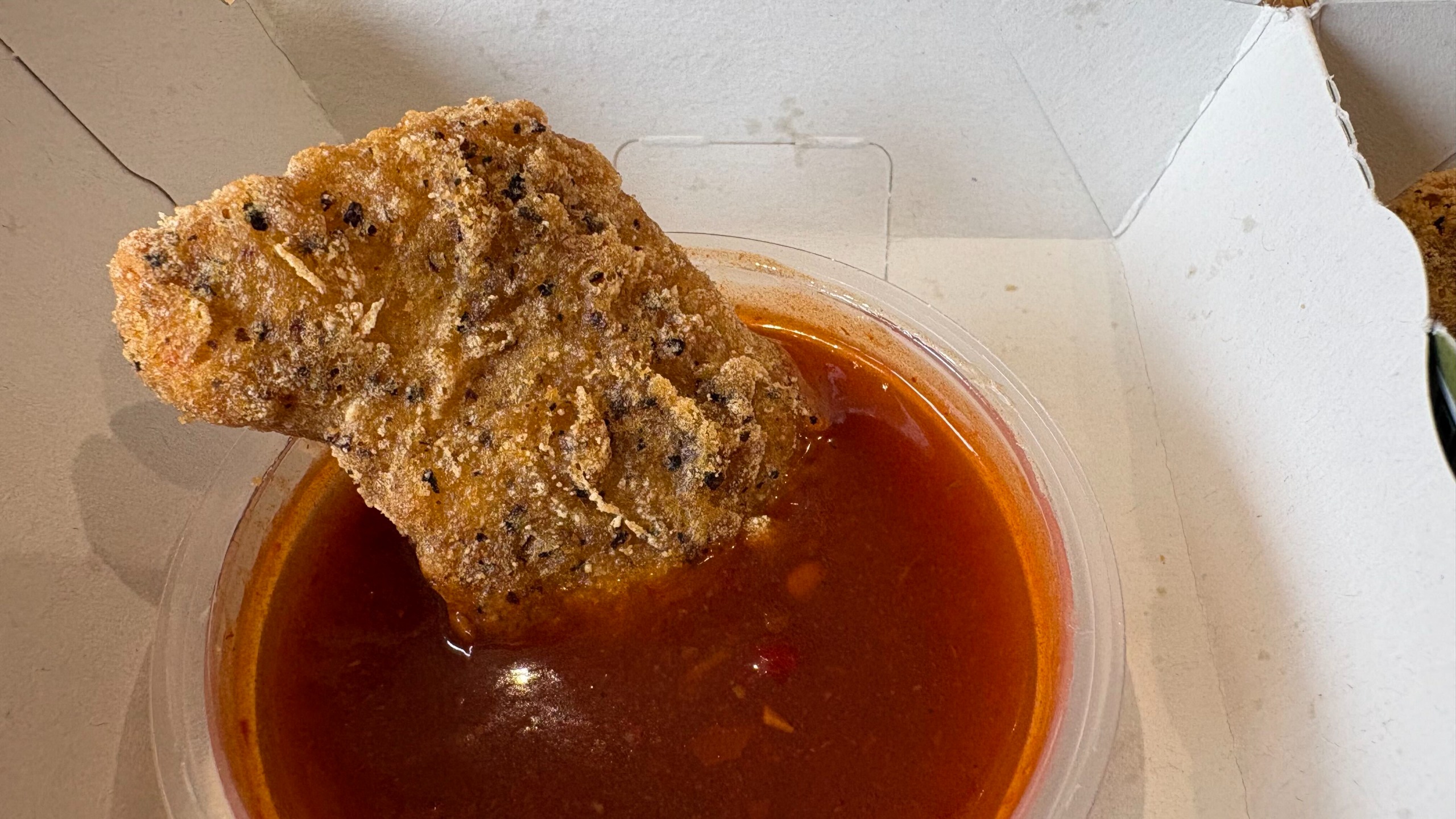 A McDonald's black pepper and garlic chicken nugget dipped into a tub of red World of Warcraft buffalo sauce.