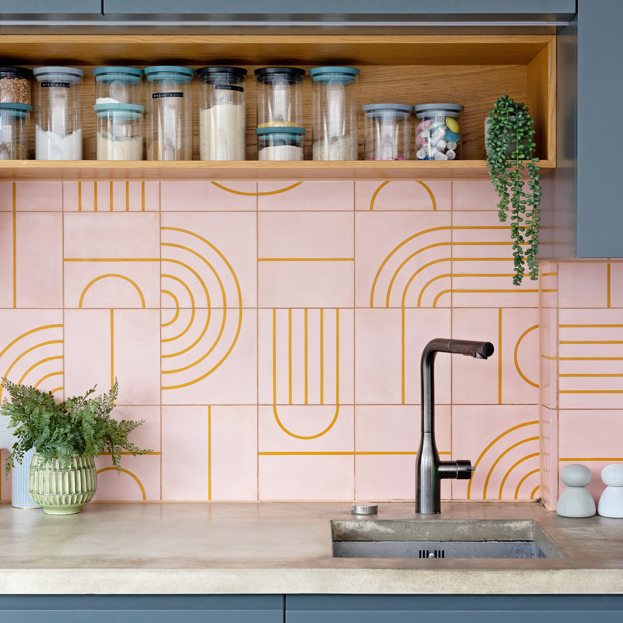 a concrete kitchen countertop with a pink tiled splashback and dark blue cabinetry