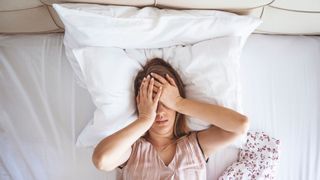 Young woman lies in bed with sleep problems cause by choosing a memory foam hybrid instead of a latex hybrid