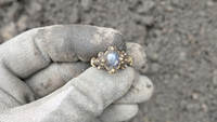 a person holds a gold ring covered in dirt with their fabric-gloved hand
