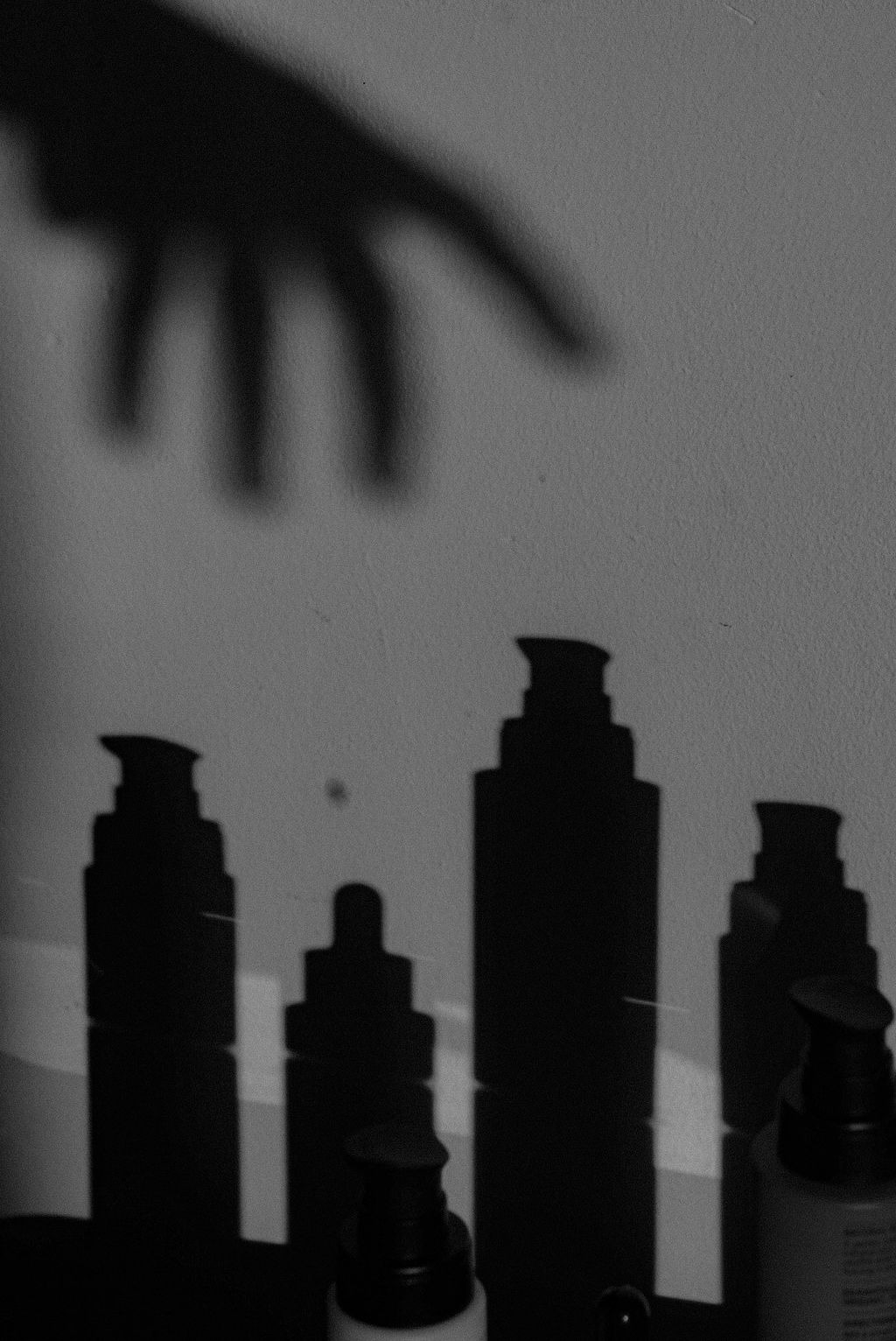 Shadows of skincare bottles cast on the wall.
