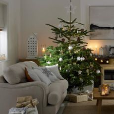 Pale grey living room, large decorated Christmas tree, grey sofa and armchair, festive cushions, wood burning stove, wooden reusable advent calendar. Pub Orig
