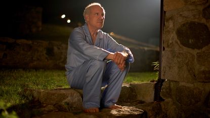 Older man sitting in the backyard at night in his pajamas