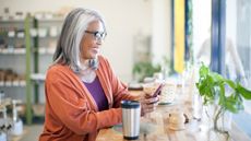 An older woman smiles while she sits in a shop and looks at her phone.