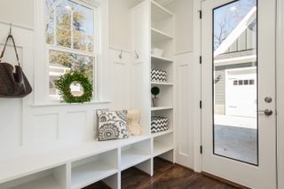A small white mudroom with a window, bench seating and a glass paneled door