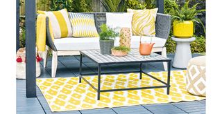 outtdoor gray decking arae with sofa and yellow outdoor rug to suggest a budget garden idea to improve floors