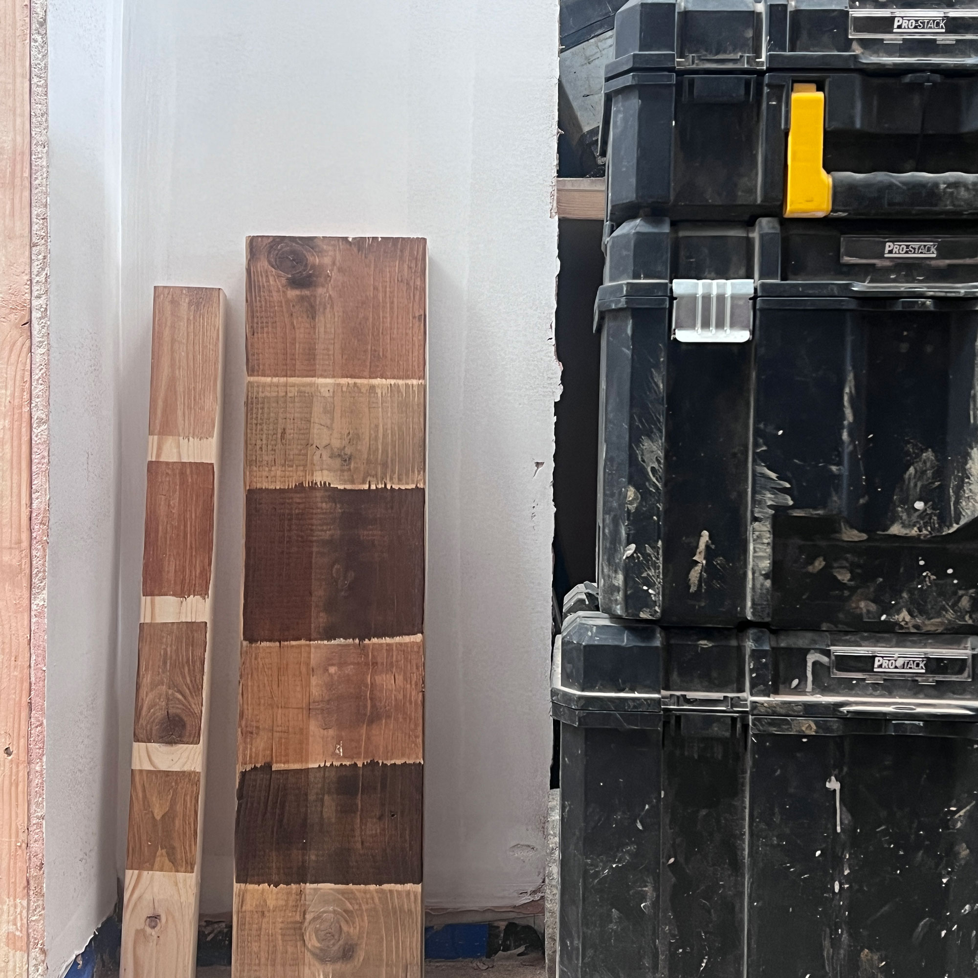 Two planks of wood showing different effects of stain, leaning against white wall
