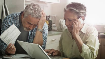 Stressed mature couple on the phone and using a laptop in the kitchen