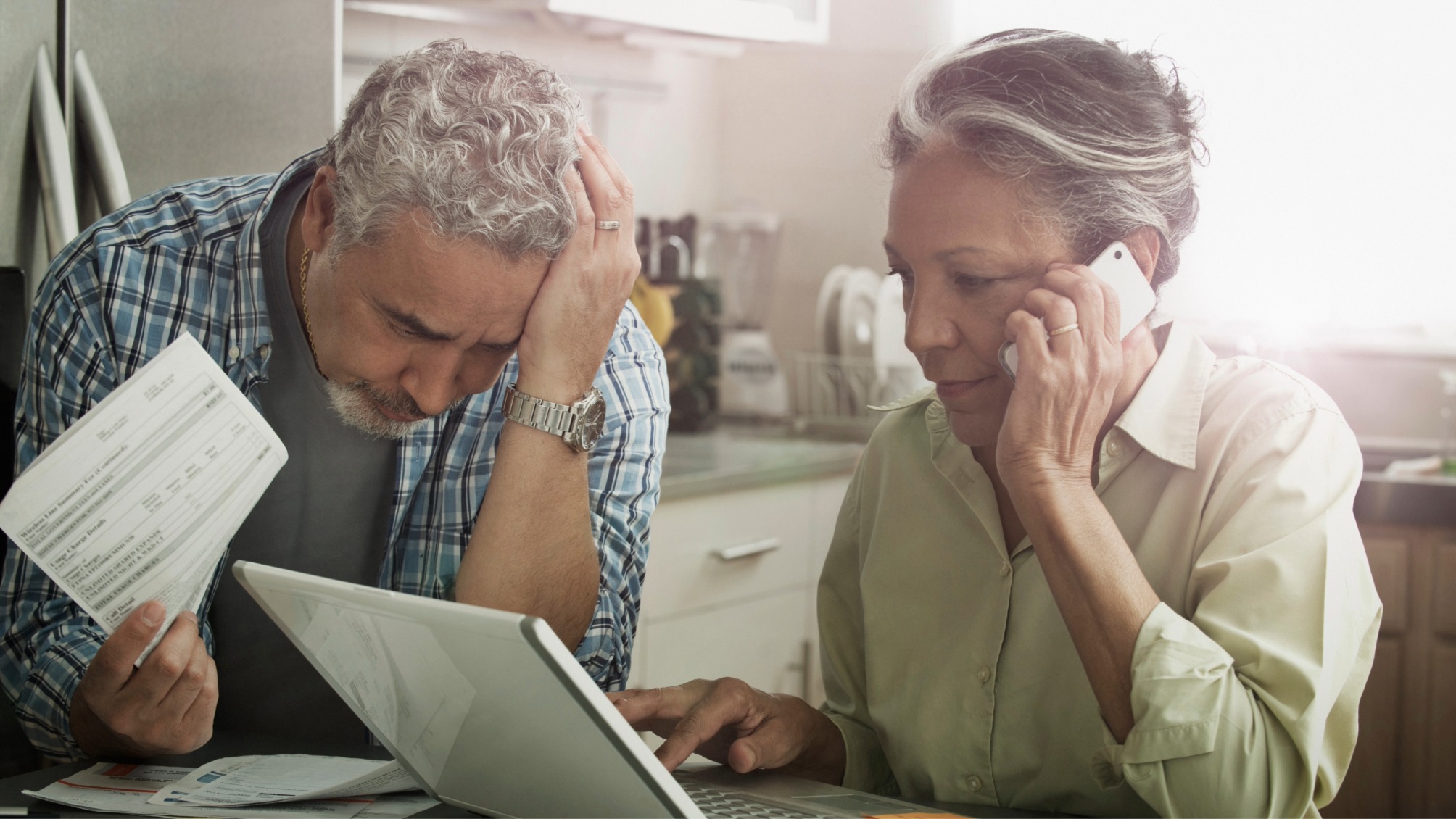 Stressed mature couple on the phone and using a laptop in the kitchen