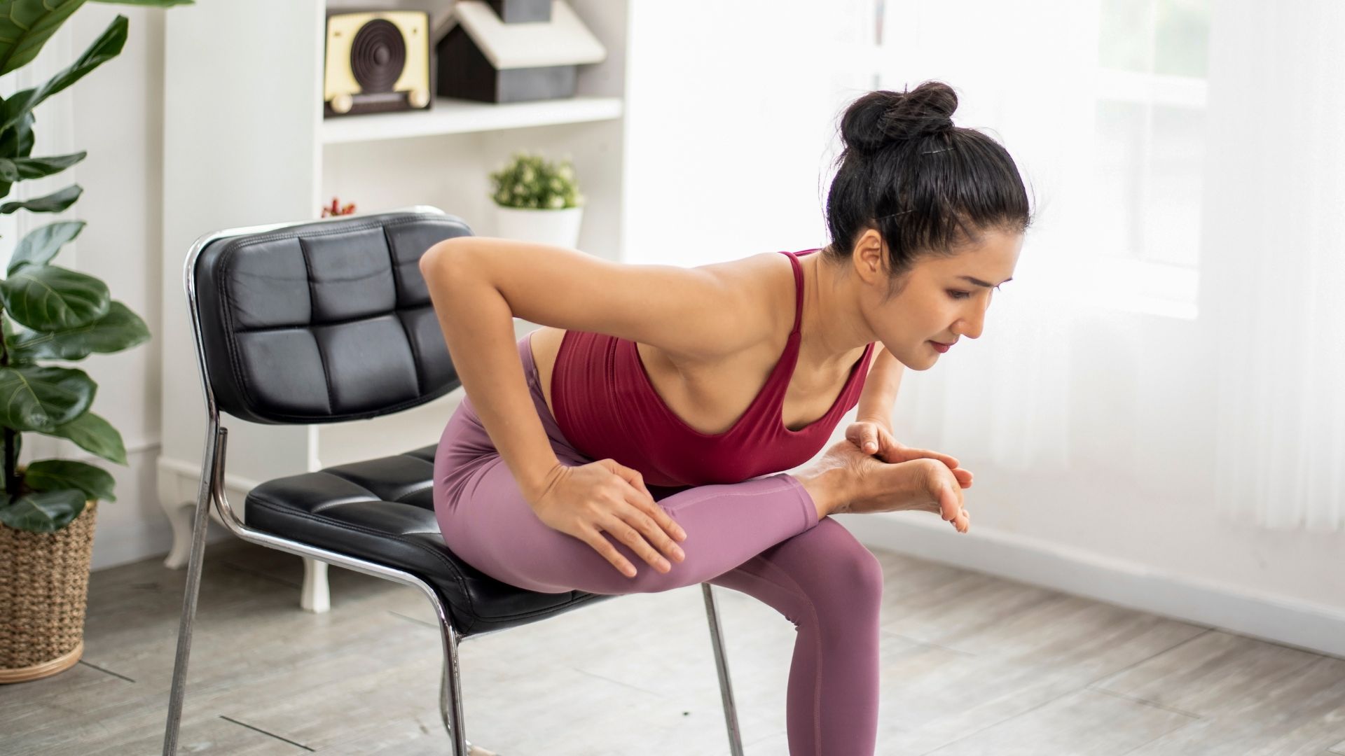 Woman demonstrating supported pigeon pose at home on chair in living room as part of a chair yoga workout