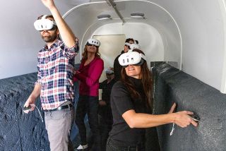 people in VR glasses walk down a white hallway lined with faux-moon-dirt walls