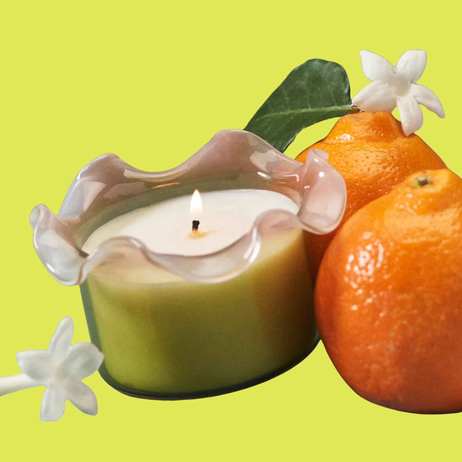 A glass candle with a ruffle rim by oranges and jasmine