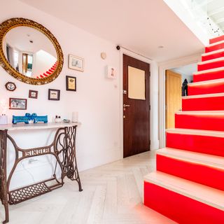 hallway with red stair and rounded mirror on wall