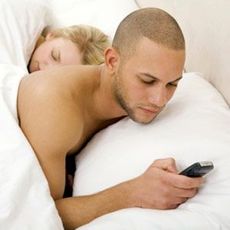 guy using a cell phone while in bed with a woman