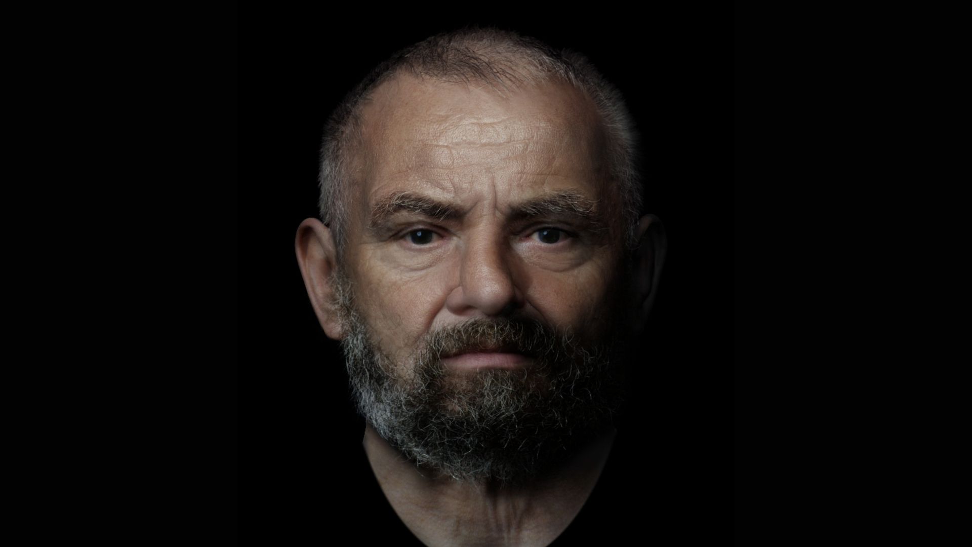 A photo of a balding man with a gray beard against a black background
