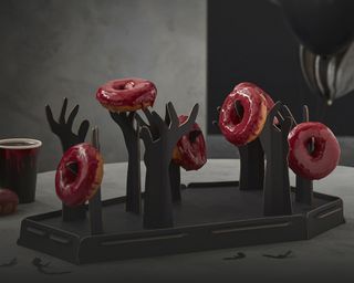 Halloween coffin and hand donut stand with assortment of glazed donuts with red icing