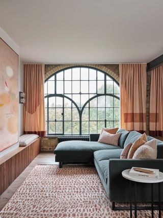 a living room with large crittal windows with peach curtains