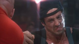 Sylvester Stallone grimacing and wearing his hat backwards while arm wrestling in Over The Top