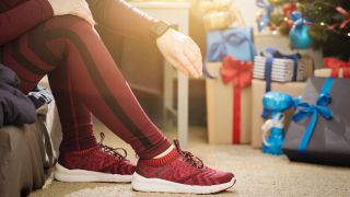 Person sitting on sofa wearing tracksuit and running watch, wrapped gifts in background