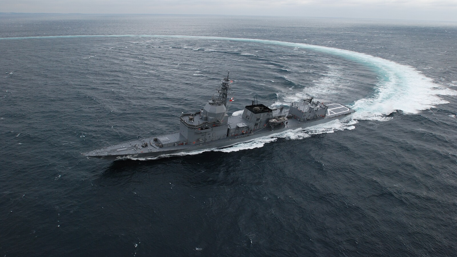 Aerial photograph of Japanese ship, JS Asuka, performing a turning maneuver in the ocean.