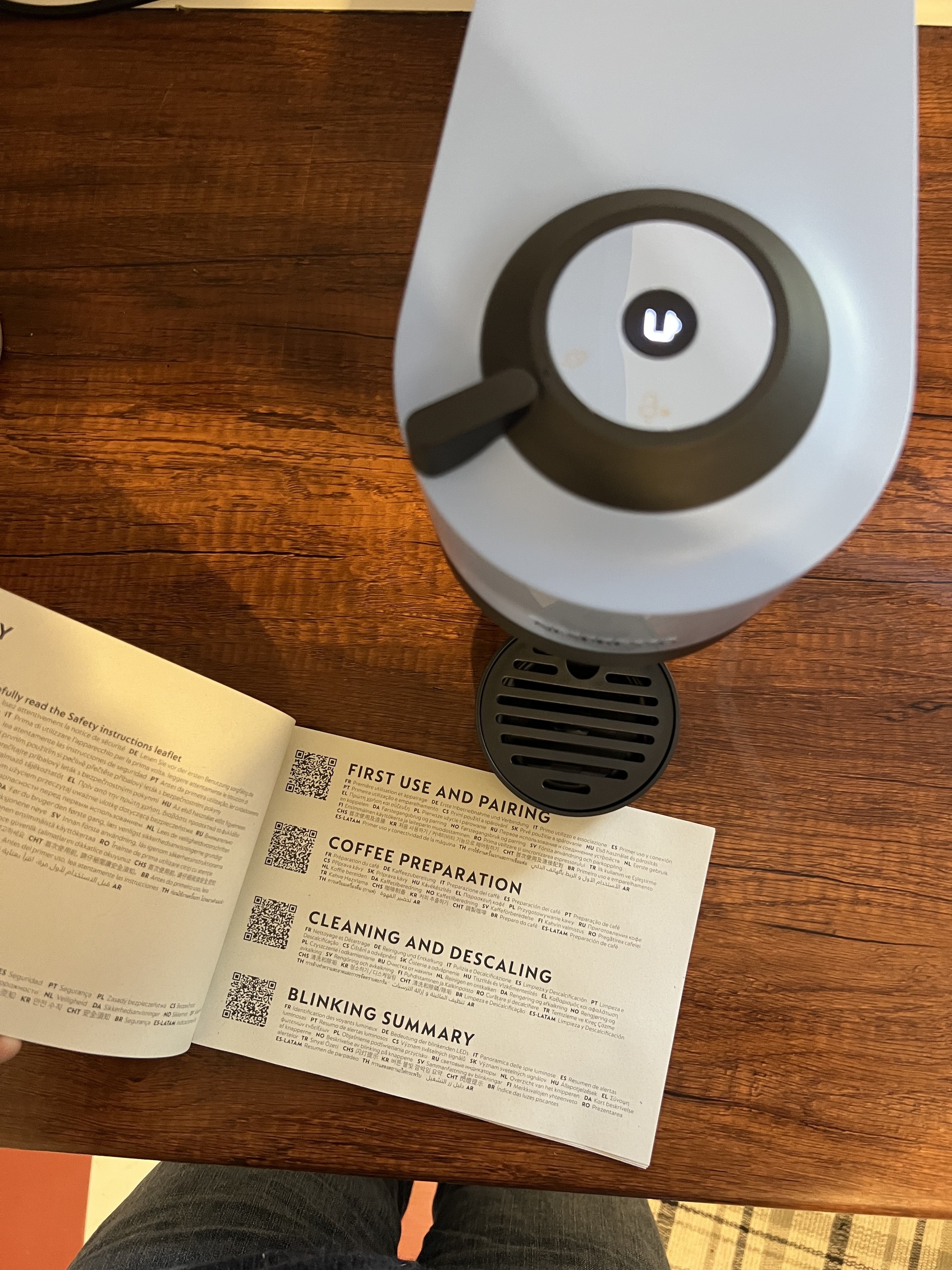 A light blue and black Vertuo Pop machine on a wooden countertop with an open instruction manual next to it.