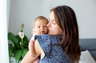 new mum holding newborn baby over her shoulder and kissing its cheek