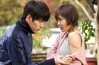 A boy holds a girl's wrist and looks at the jagged cut on her arm, in a still from the 2010 k-drama 'Secret Garden.'