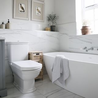 White walled marble bathroom with white bathtub, toilet, and wall art