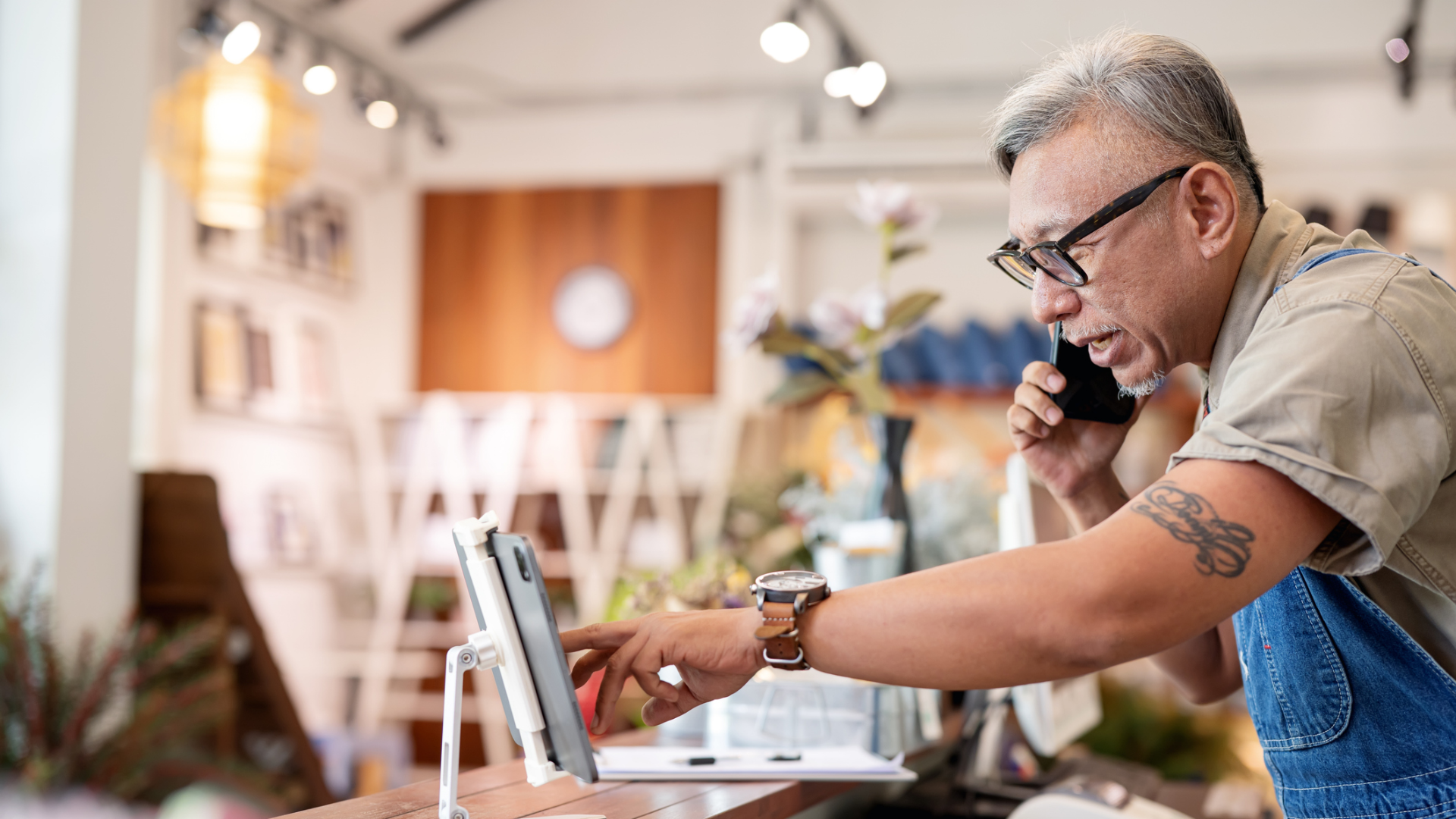A shopkeeper talking on the phone to a customer while checking stock on a tablet