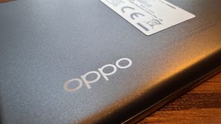 A silvery grey Oppo Reno10 camera phone sitting on a wooden table