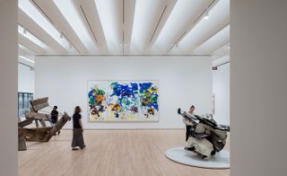 Interior view of a gallery space at The San Francisco Museum of Modern Art (SFMoMA) featuring white walls, wood flooring and a collection of colourful paintings on the wall. There are also two pieces of art on display, a wooden structure and a white and metal structure