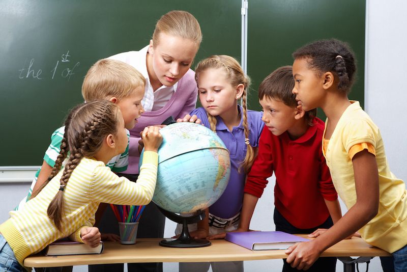 Kids gather together to look at a globe with their teacher.