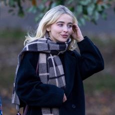 Sabrina Carpenter wearing a black Aritiza coat, plaid scarf, jeans, and a burgundy Celine bag in Central Park