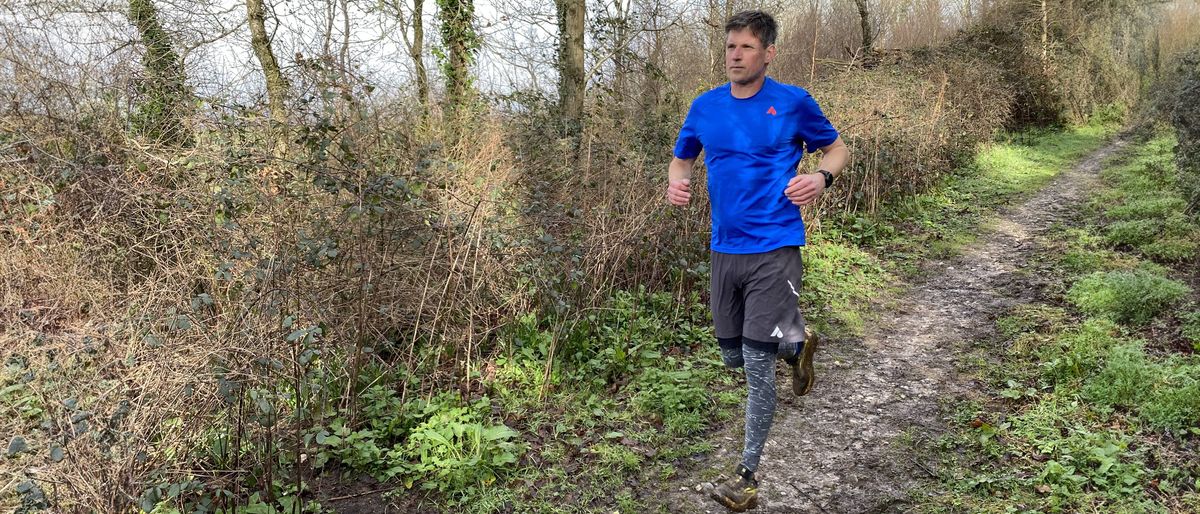 A man wearing Saxx Roast Master Mid-Weight Tights runs along a woody trail