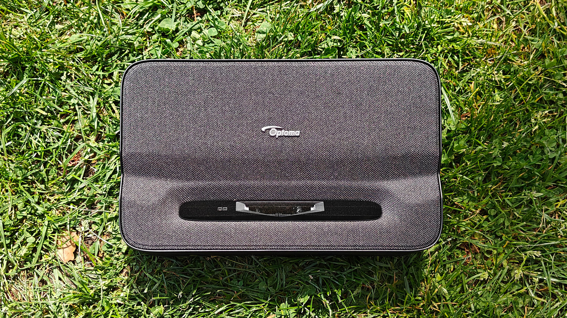 Optoma Photon Go portable UST projector sitting on grassy lawn top down view showing lens aperture and Optoma logo