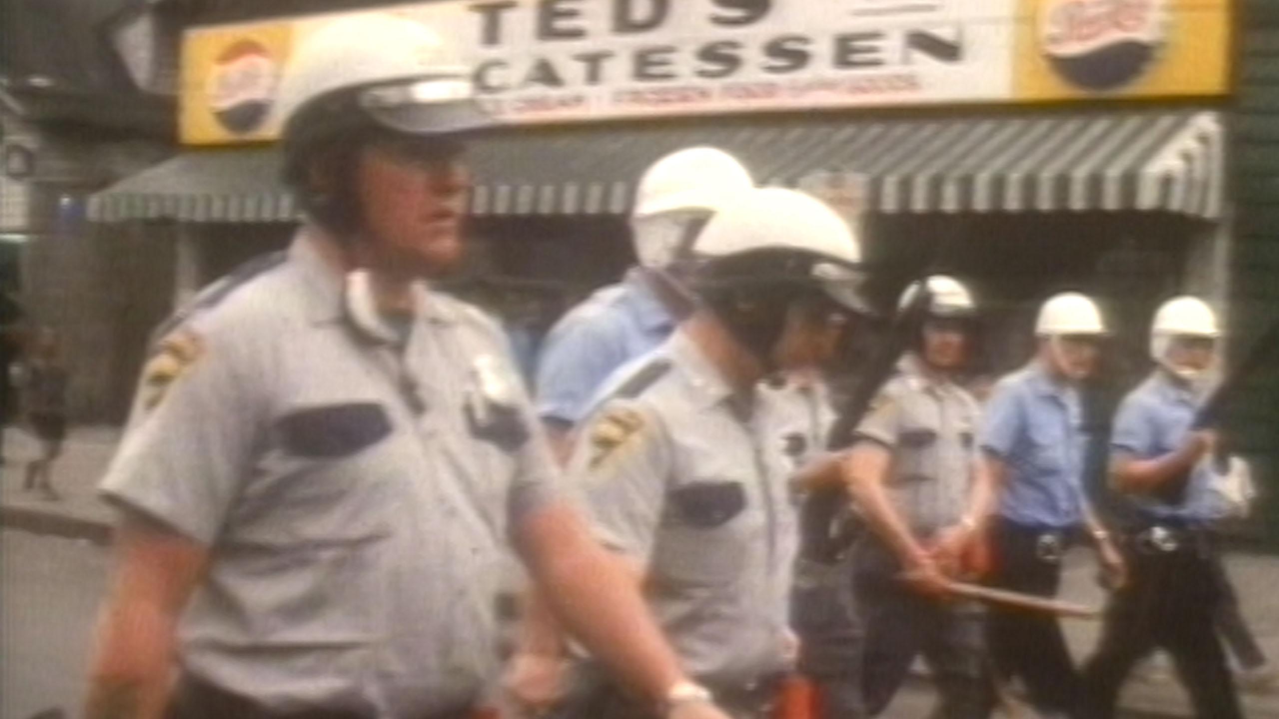 an archival photo of a group of policemen wearing helmets, walking in front of a deli