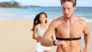 Half-naked man running on a beach wearing a heart rate monitor
