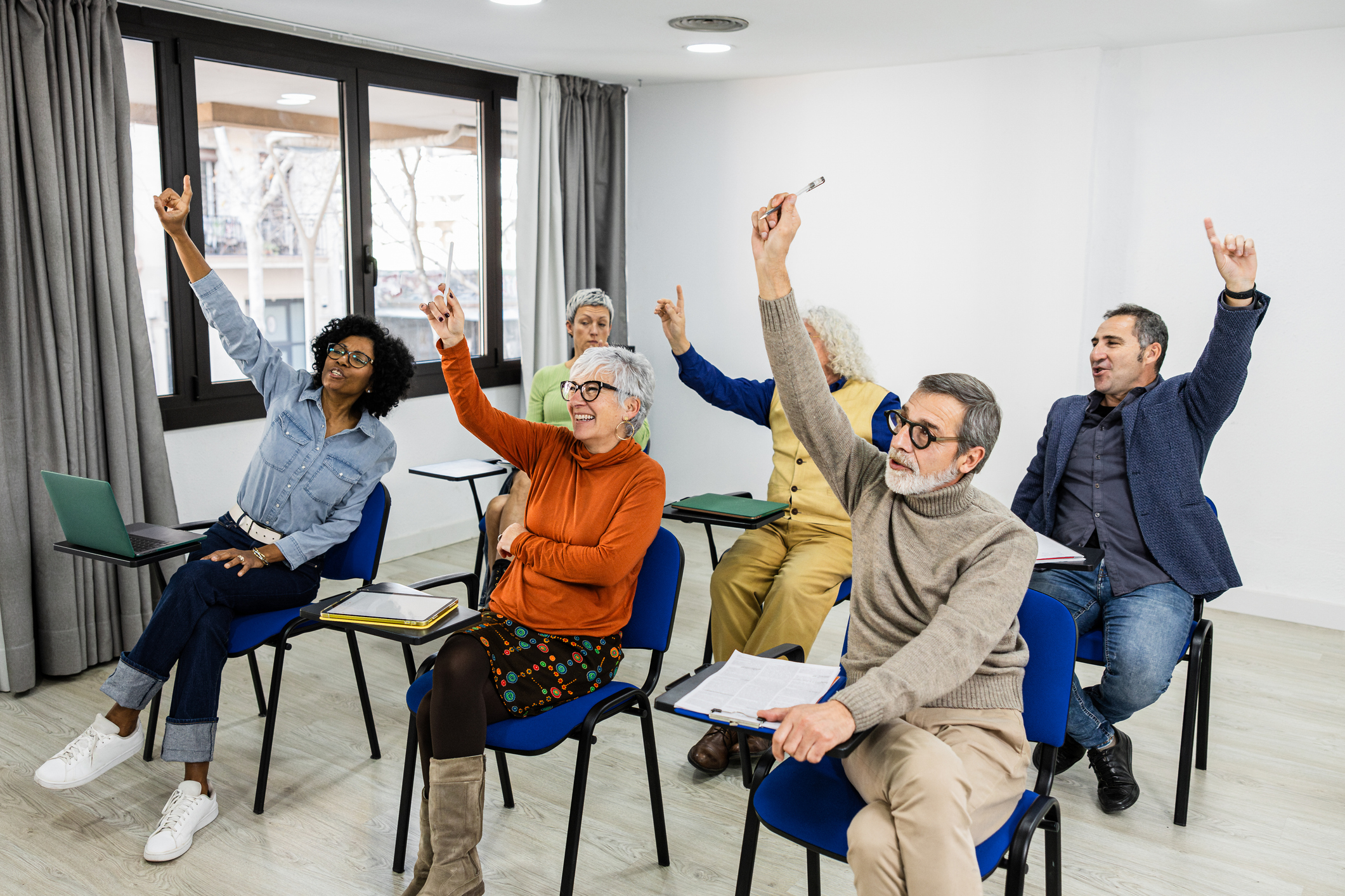 adult school, all students with their hands raised, sitting at their desks.