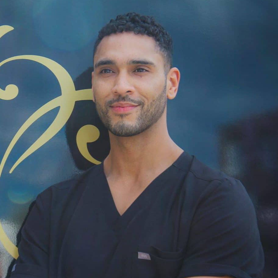 Image of Dr Richard Devine, leading Aesthetic Doctor, from Devine Clinic, smiling and wearing black V-neck scrubs