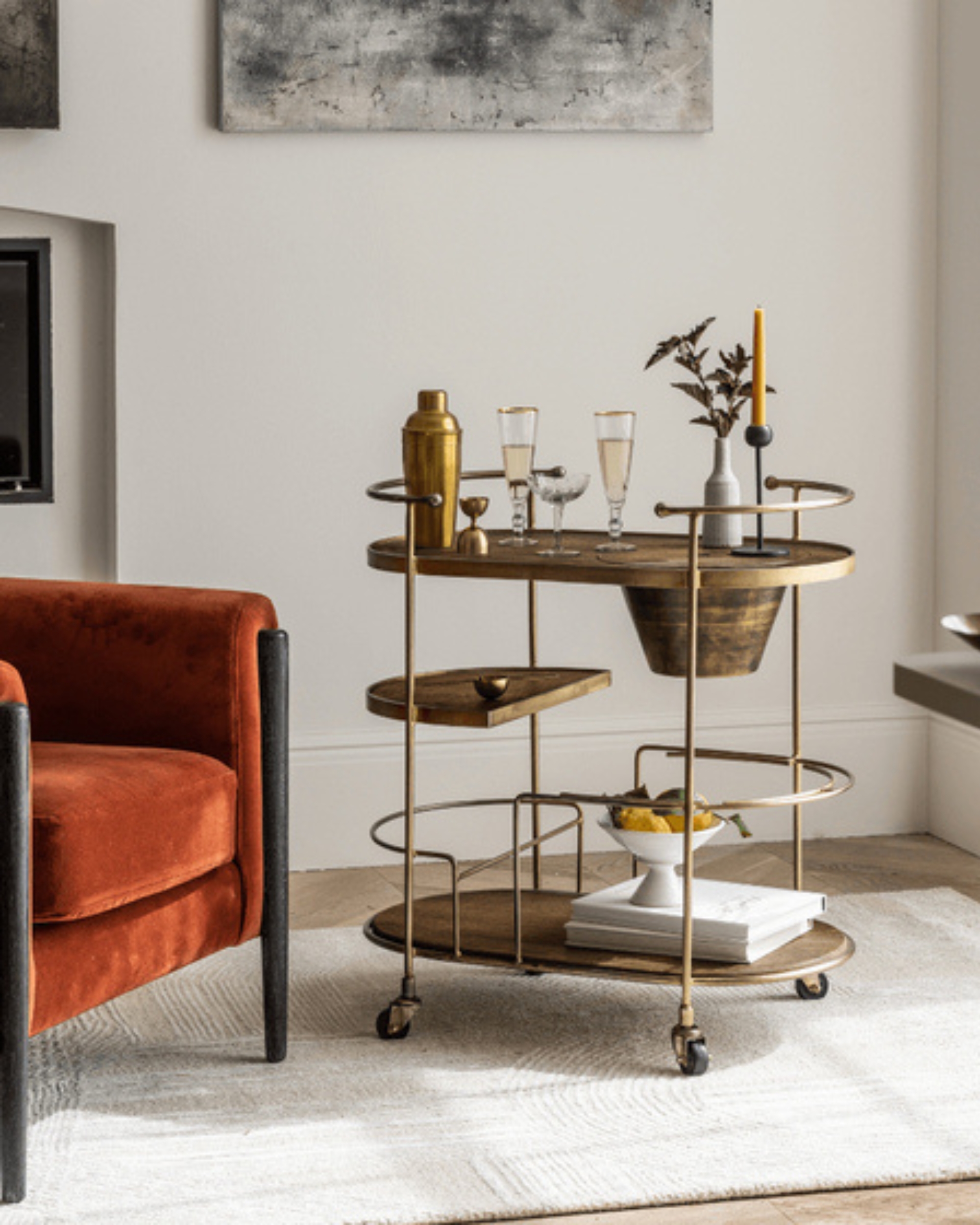 Image of an antiqued gold bar cart in a white living room next to a velvet red accent chair.