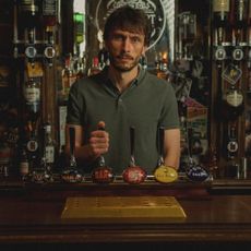 a man (richard Gadd as donny dunn) stands behind a bar with his hand on a tap handle, in netflix's 'baby reindeer'