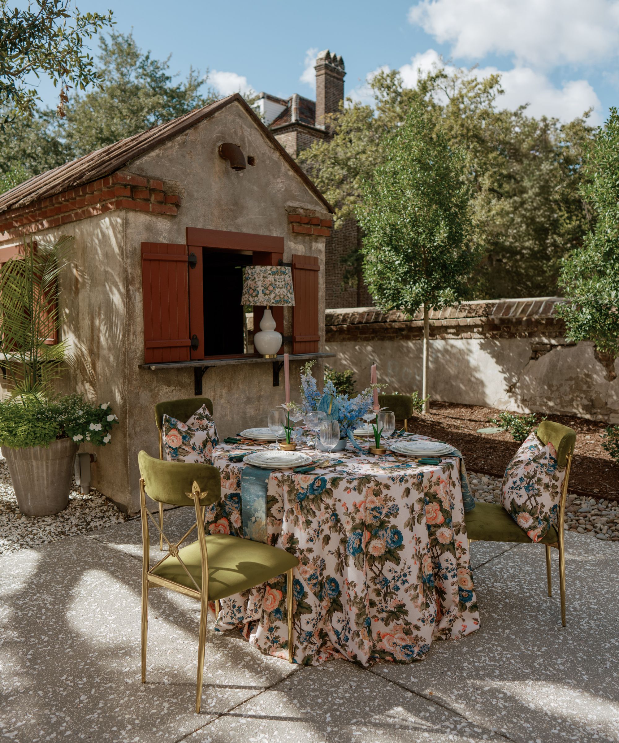 Outdoor table with a floral tablecloth, green velvet seats and a blue floral centerpiece