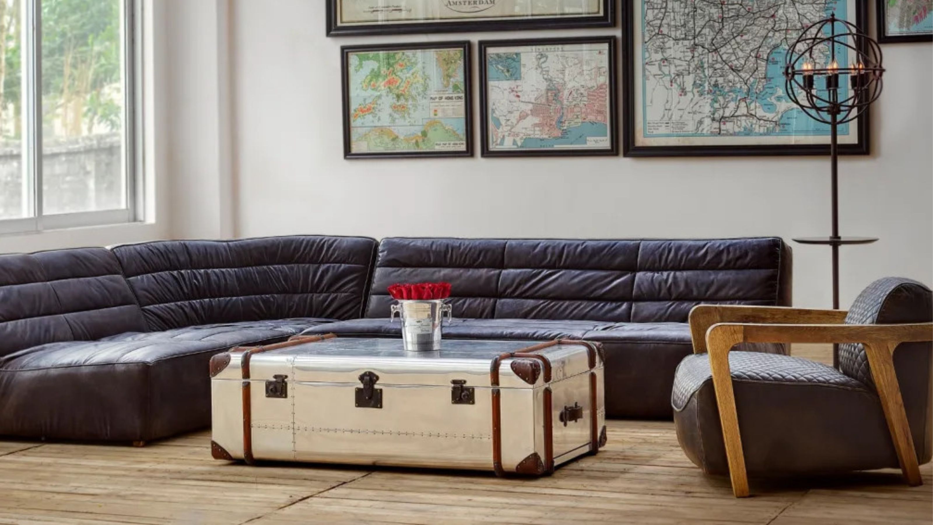 living room with leather curved sofa, timber floors, an armchair, gallery wall of maps, and metal storage trunk as the coffee table