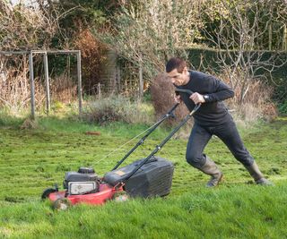 First lawn cut of the year struggling after the mild winter and long grass growth on a lawn mowing with a petrol cutter