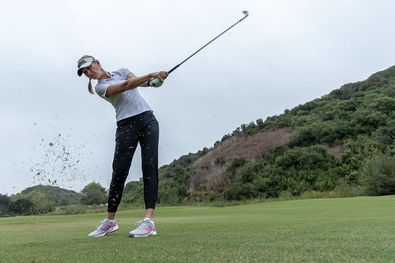 A woman wearing adidas golf apparel putting on the course
