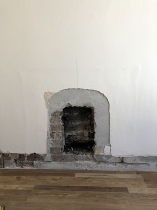 A hole in a wall where a fireplace insert would fit with a wood floor beneath it