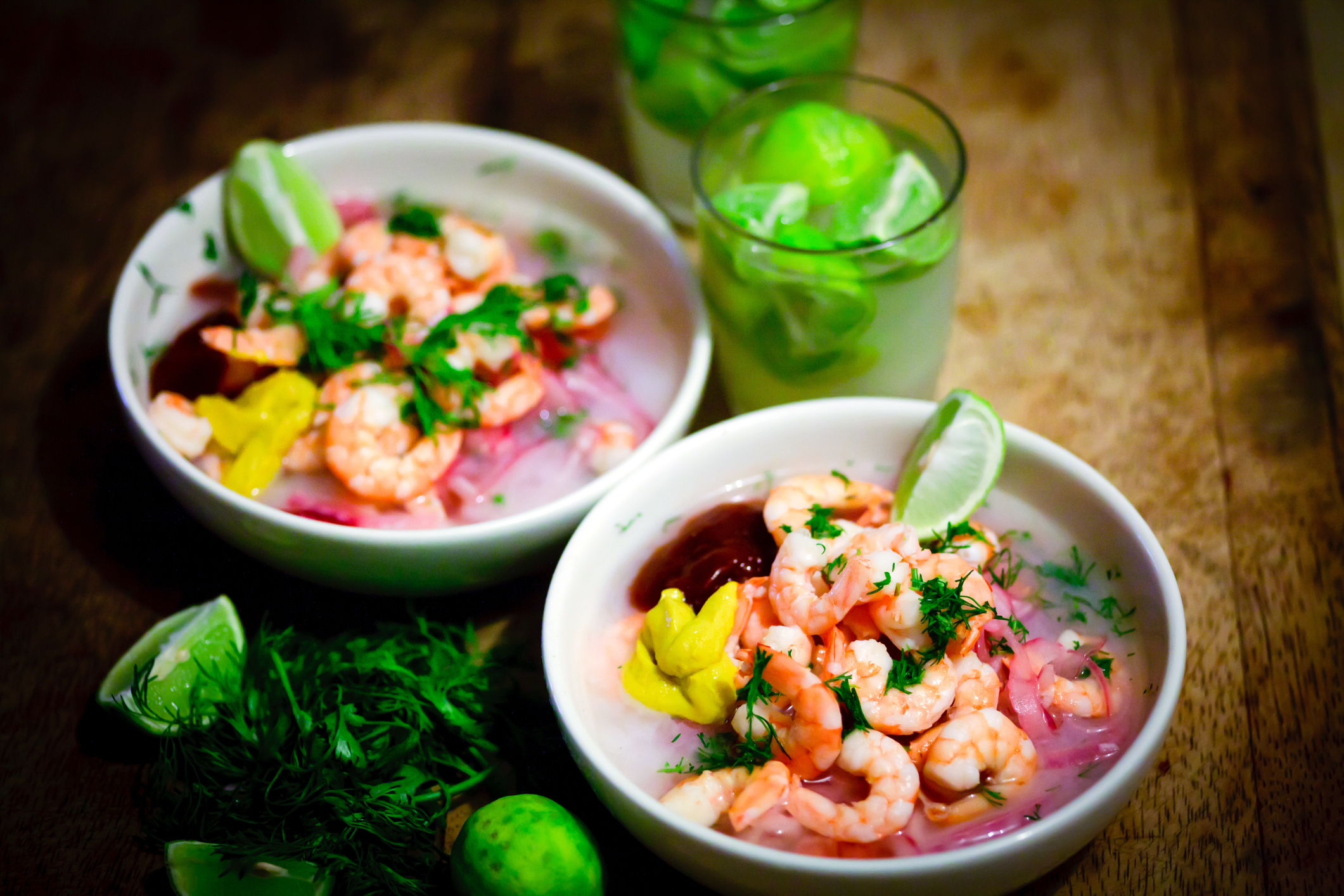 Two bowls of shrimp ceviche with wedges of lime.
