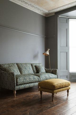 Green patterned sofa in grey room with wooden floor and yellow footstool