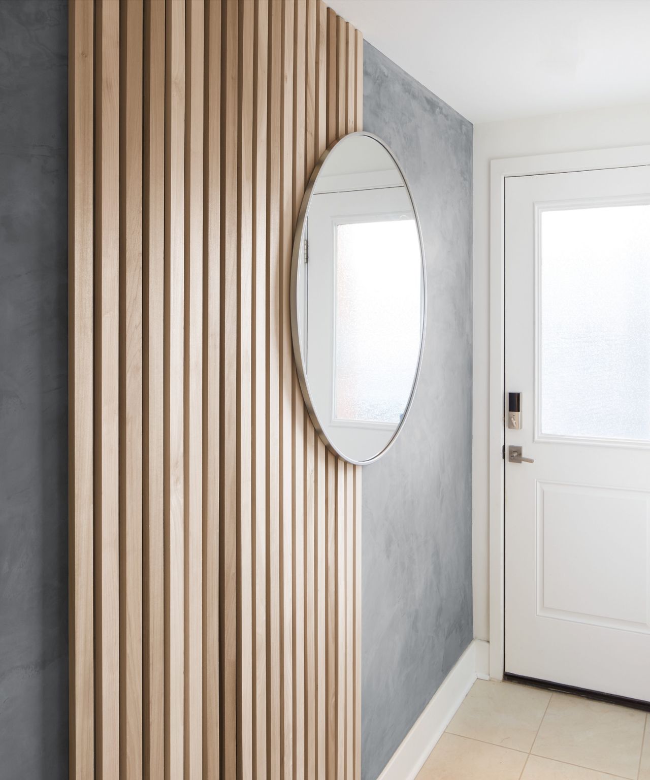 Wooden slat wall paneling in entryway with round mirror hung on grey painted wall