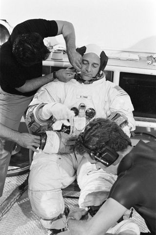 Ronald E. Evans sits while staff prepare him for EVA training in the water tank. He is wearing a spacesuit and is yet to put his helmet on.